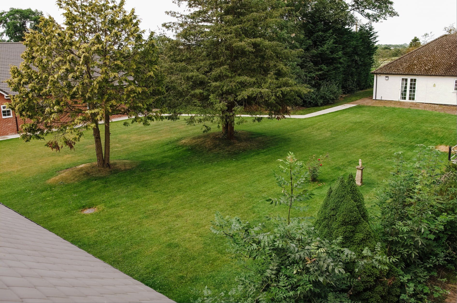 A wide lawn with mature trees and a path, with Highbarrow buildings at the edges.